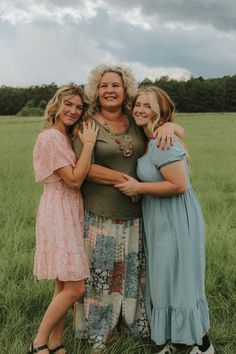 three women standing together in a field with their arms around each other and smiling at the camera