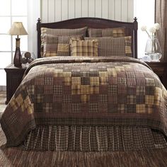 a bed in a bedroom with brown and tan plaid bedspread, pillows and lamps