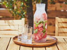 a wooden tray topped with a bottle filled with watermelon next to two glasses