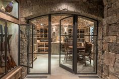 an arched glass door leads into a wine cellar with stone walls and floor to ceiling windows