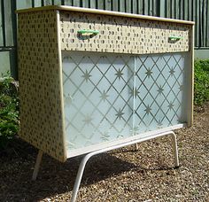 a white cabinet sitting on top of a metal stand in front of a fence and bushes