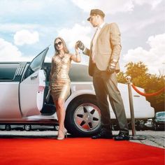 a man standing next to a woman in front of a white car on a red carpet