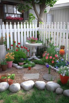 a white picket fence with flowers and rocks in the yard next to a small garden