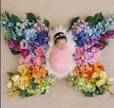 a baby wrapped in a pink blanket surrounded by colorful flowers and greenery on a beige background