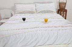 two glasses of orange juice sit on a bed with white linens and wicker chairs