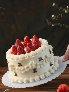 a cake with white frosting and fresh strawberries on top is being held by a hand