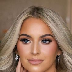 a woman with blonde hair and blue eyes is posing for the camera, her hand on her face