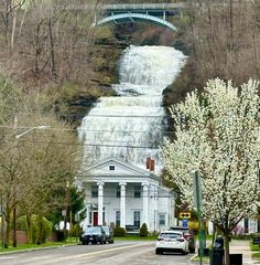 a white house with a waterfall in the background and cars parked on the side of the road