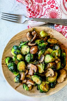 a wooden bowl filled with brussel sprouts and mushrooms next to a fork