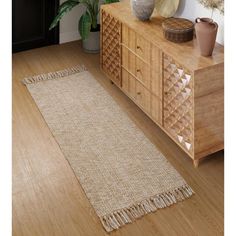 a large rug with fringes is on the floor next to a dresser and potted plant