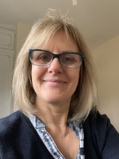 a woman with glasses is smiling for the camera while wearing a blue sweater and plaid shirt