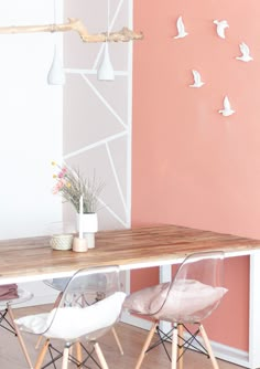 a dining room table with two chairs and a vase on top of it, in front of a pink wall