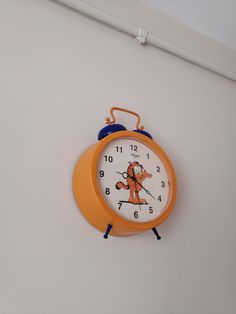 an orange and white clock hanging on the wall with mickey mouse painted on it's face