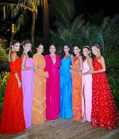 a group of women standing next to each other on a wooden platform in front of palm trees