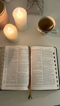 an open book sitting on top of a table next to two candles and a cup of tea