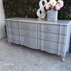 a gray dresser with flowers and a clock on top