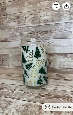 a white candle with green and gold christmas trees on it sitting on a wooden surface