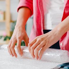 a woman is rolling up some food on a counter top with plastic wrap around her hands