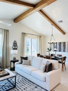 a living room filled with white furniture and lots of wood beaming on the ceiling