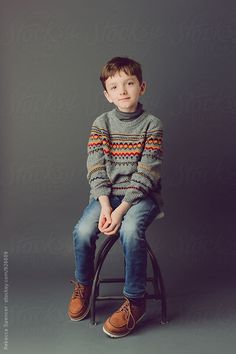 a young boy sitting on top of a stool wearing a sweater and jeans by luke van deren for stockstation