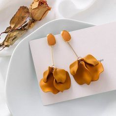 a pair of yellow flower shaped earrings sitting on top of a white plate next to a leaf