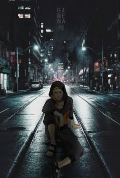 a woman sitting on the ground in an empty city street at night with buildings lit up behind her