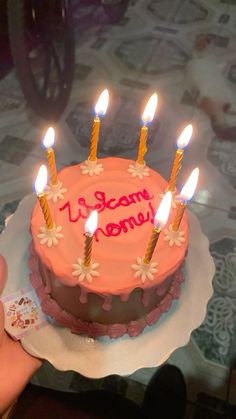 a pink birthday cake with five lit candles