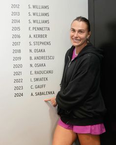 a woman standing in front of a wall with names on it and pointing to the side