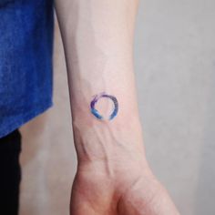 a woman's wrist with a small blue circle tattoo on the left side of her arm