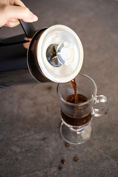 someone is pouring coffee into a glass mug