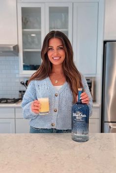 a woman is holding a glass and bottle in her hand while standing at the kitchen counter