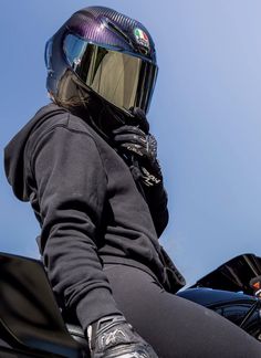 a person wearing a helmet sitting on top of a black motorcycle parked in front of a blue sky