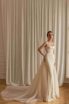 a woman standing in front of a white curtain wearing a wedding dress with an open back