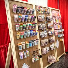 a display case filled with lots of different colored pens and pencils next to a red curtain