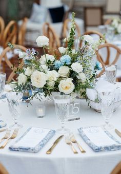 the table is set with white and blue flowers, silverware, and napkins