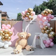 a teddy bear sitting in front of a balloon arch