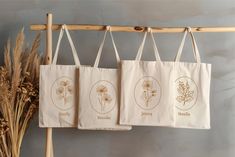 three tote bags hanging from a wooden rack next to dried flowers and plants on the wall