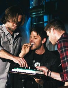 three men standing around a cake with candles on it