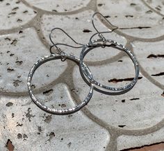 These hoop earrings are entirely hand-made of sterling silver wire. The hoops were formed by hand, soldered, and then given a bark-like texture with the edge of my favorite hammer. In the photos showing two pairs of earrings the medium size (for this listing) are the larger ones shown at the top of the photo. MEASUREMENTS These earrings each measure 2" long from the top of the hook. Each circle measures 1 & 3/8"" in diameter. Artisan made, with love, in my small home studio in Springfield, Oregon. Made by own hands from sterling silver wire, smithing tools and fire. If you have any questions about individual pieces, or my process, please feel free to ask me using the contact seller button. I'm happy to answer them. If you would like to see more of my silver work please visit my shop here: Artisan Small Hoop Sterling Silver Earrings, Silver Artisan Hoop Earrings Nickel Free, Artisan Silver Nickel-free Hoop Earrings, Adjustable Soldered Hoop Earrings For Gifts, Small Metal Hoop Earrings With Soldered Detail, Small Hoop Metal Earrings With Soldered Details, Gift Hoop Earrings With Soldered Metal, Nickel-free Adjustable Silver-plated Hoop Earrings, Hand Forged Sterling Silver Hoop Earrings