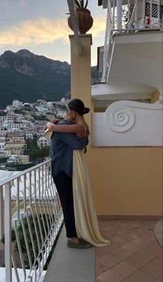 a woman standing on top of a balcony next to a tall white building with buildings in the background