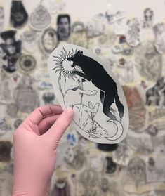 a hand holding up a sticker with a cat on it's face and another drawing in the background