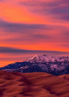 the mountains are covered in snow as the sun sets over the sand dunes and hills