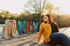 a woman sitting on a wooden bench next to clothes hanging from a line over water