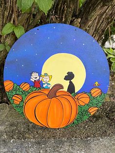 a painted pumpkin sitting on top of a cement ground next to a tree and bushes