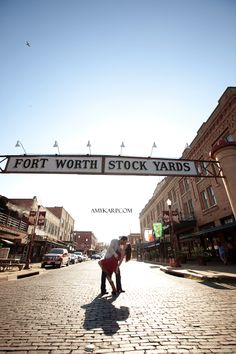 two people standing under a sign that says fort worth stock yards on the side of a street