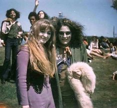 two women standing next to each other in front of a group of people on the grass