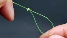 a person is holding a string with a small green thread on it and the end of the string has a tiny knot attached to it