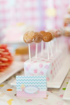 two donuts are on top of small pops in a pink and white paper box