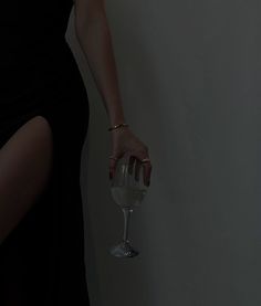 a woman's hand holding a wine glass in front of a white wall,