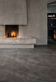 a fire place in the middle of a room with concrete walls and flooring on both sides